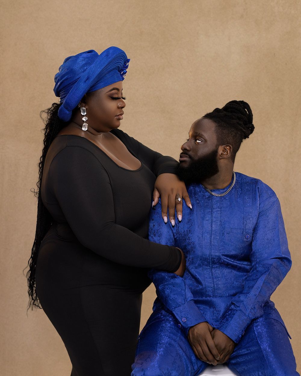 An intimate portrait of a couple wearing black and blue outfits while posing against a beige background.