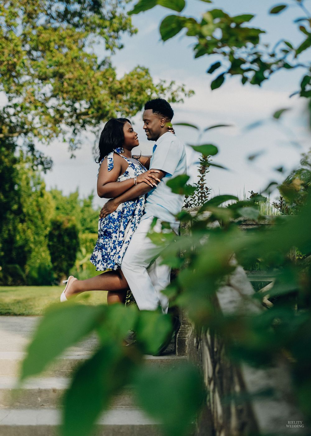 A couple embraces in a romantic outdoor photoshoot with green foliage and trees in the background.