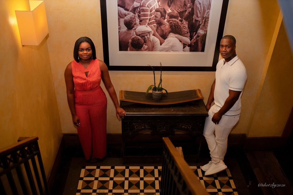 A couple stands near a framed black and white photograph in an elegant hallway setting.