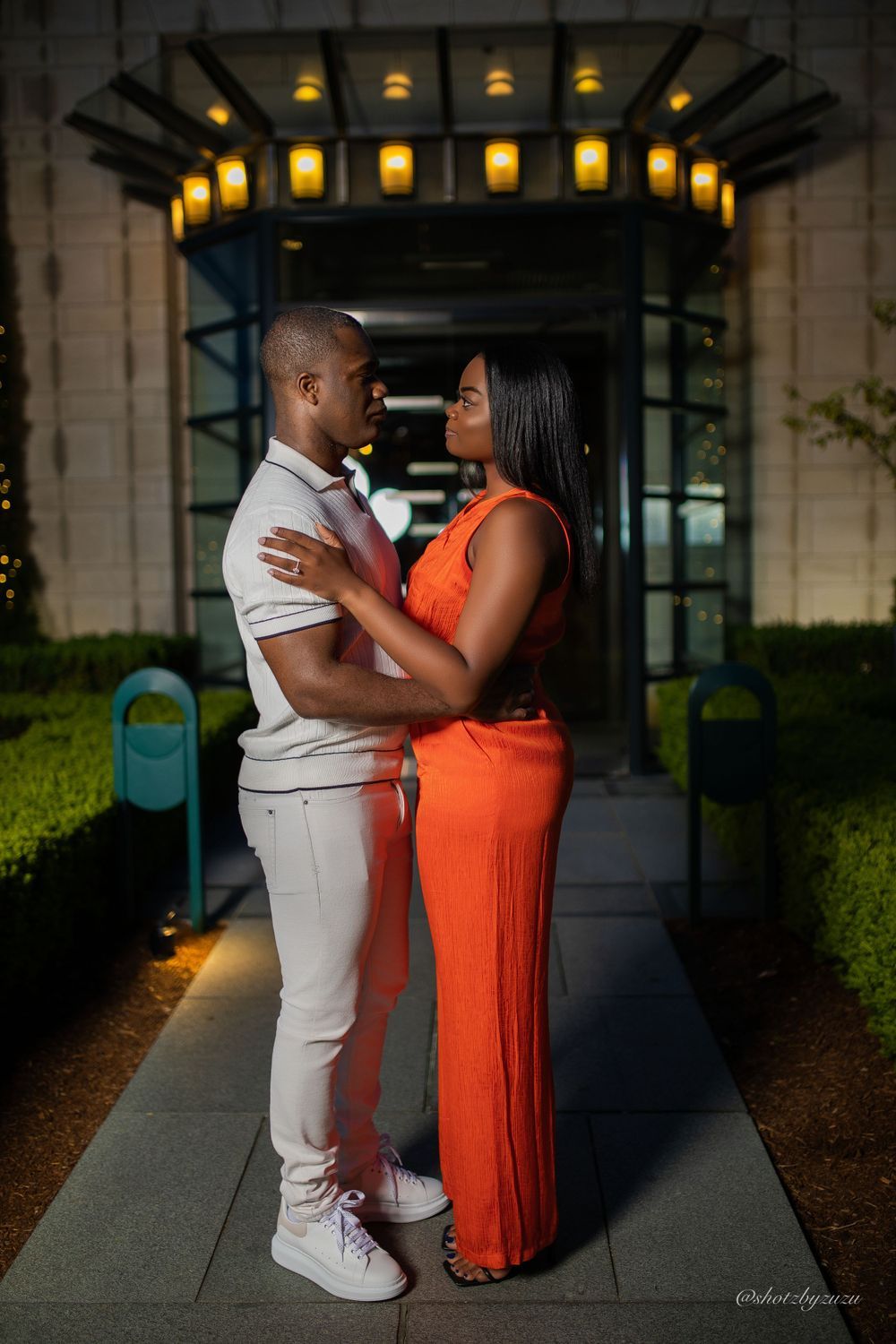 A couple embraces under illuminated archway during evening photoshoot.