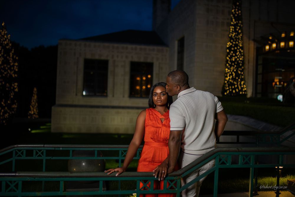 A couple sharing an intimate moment at dusk with decorative lights in the background.