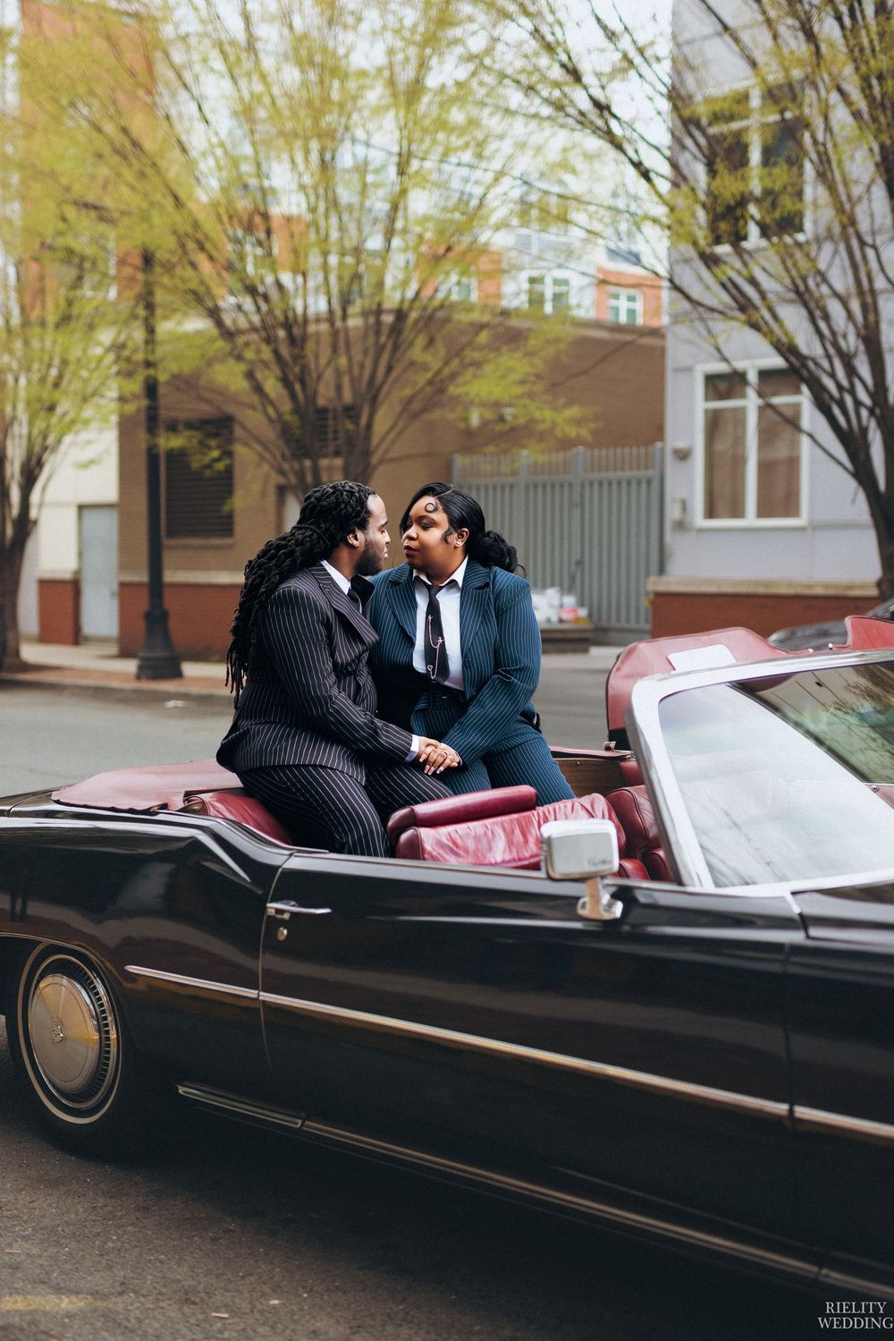 A romantic couple shares intimate moments in a classic black convertible car on a city street.