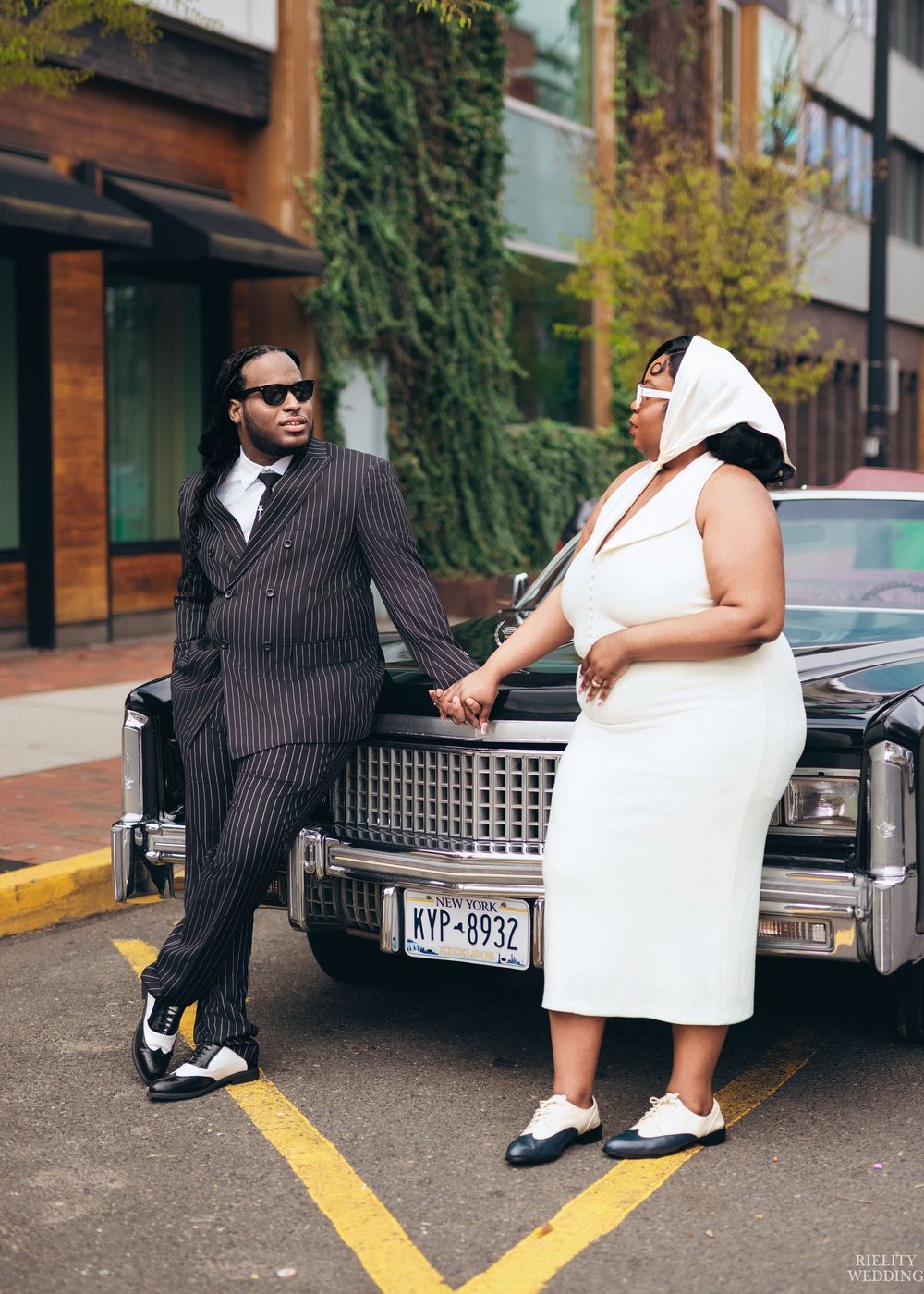 A couple in formal attire poses together near a vintage Cadillac for a stylish photo shoot.