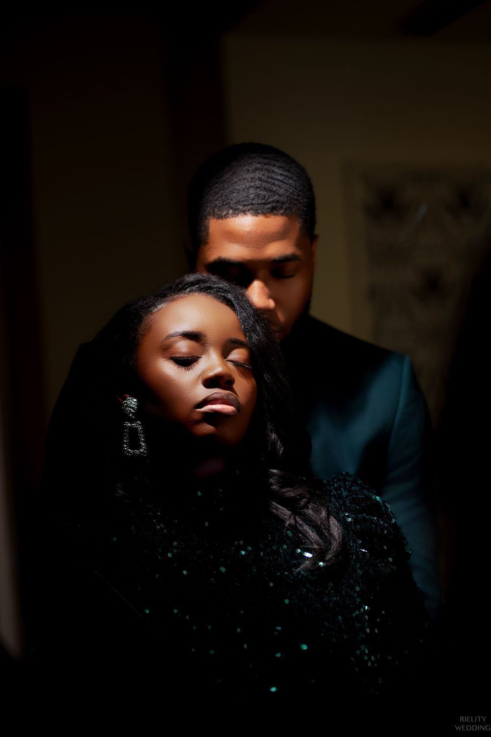 Dramatic shadowy portrait of couple in dark formal wear with moody lighting.