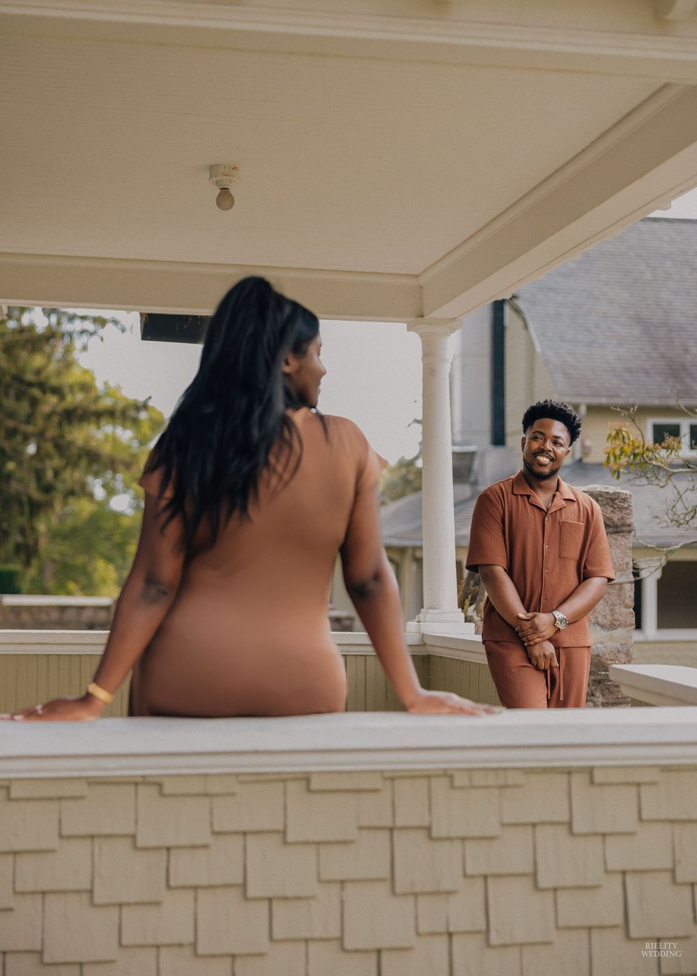 A couple shares a romantic moment on a stone porch during an outdoor photoshoot.