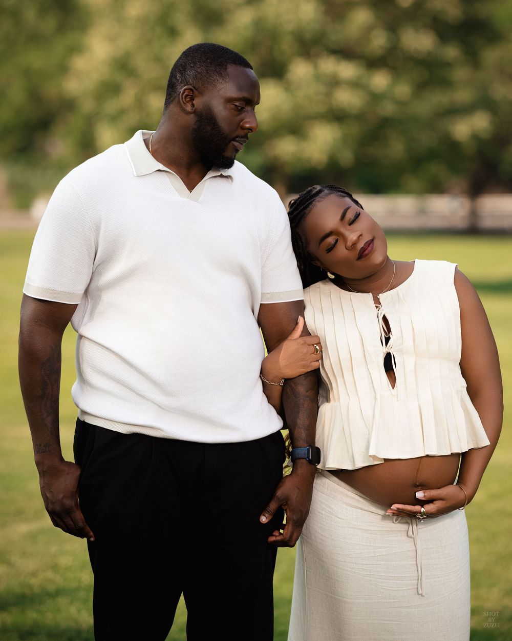 Romantic couple in black and white outfits share tender moments during an outdoor photoshoot in a sunlit garden.