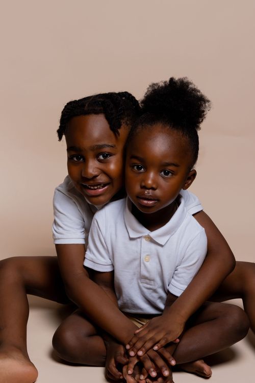 Two young children in white polo shirts sitting together against neutral background.