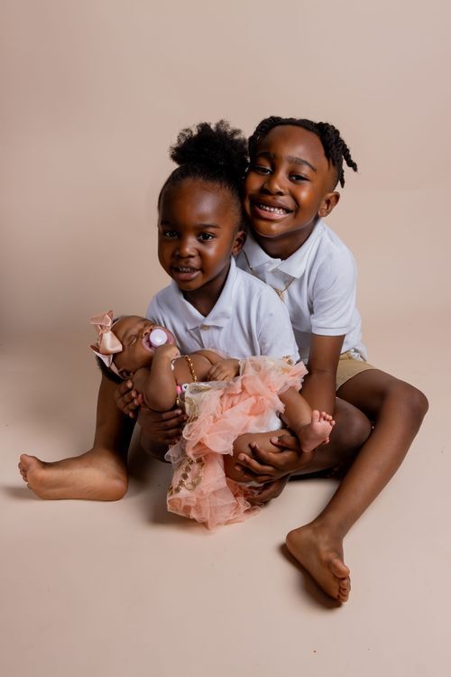 Two children in white polo shirts sitting together on beige backdrop with pink tulle.