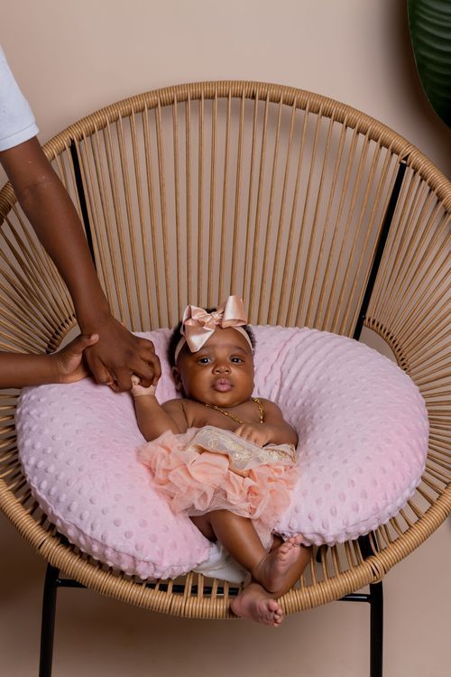Modern rattan chair with pink cushion and baby in pink outfit.