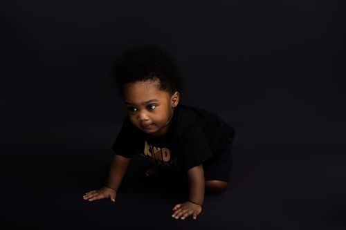 Low-light artistic portrait of small child crawling against dark background.