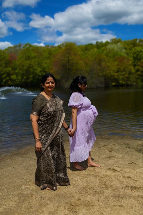 Two people in traditional and modern dress standing by lakeside on sunny day.