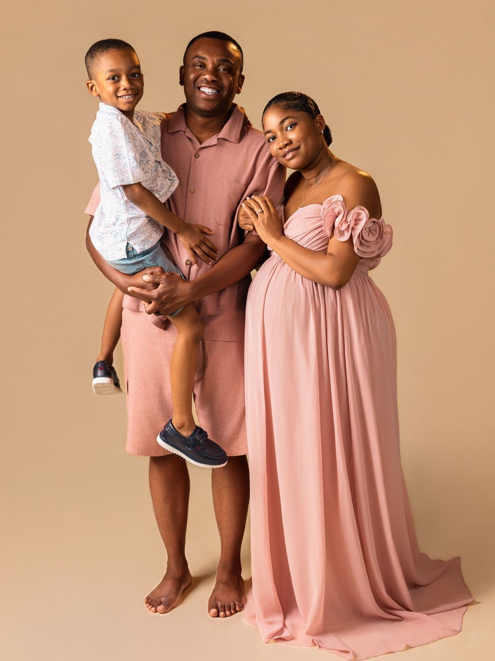 A loving family shares tender moments while wearing coordinated pink and neutral outfits in a studio setting.