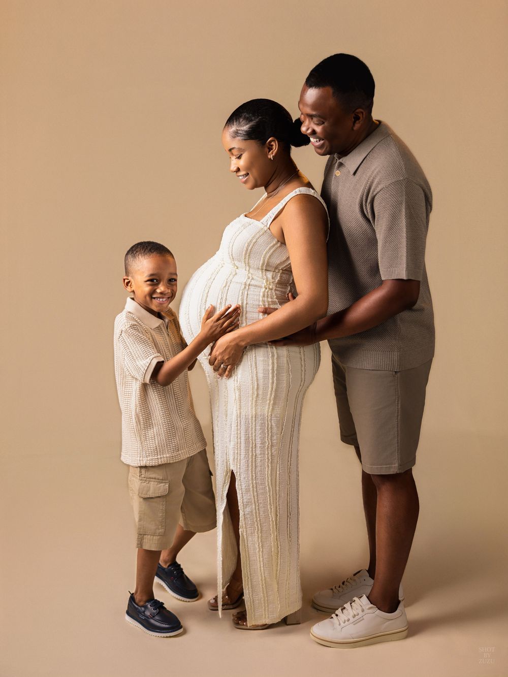A family of three in neutral tones poses together against a beige backdrop in a series of intimate portraits.