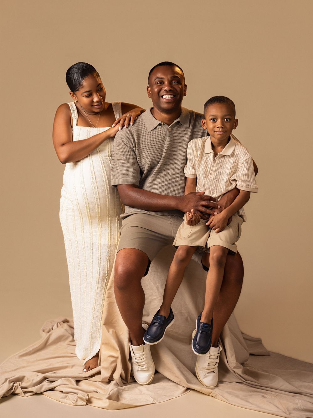 A family poses together in neutral tones against a beige backdrop for a minimalist studio portrait session.