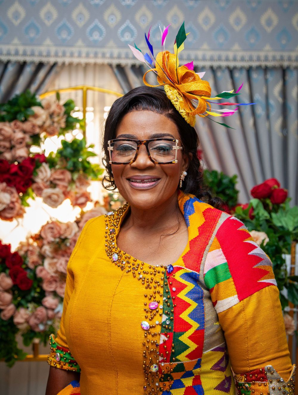 Bright yellow and multicolored traditional outfit with floral headpiece against decorative backdrop.