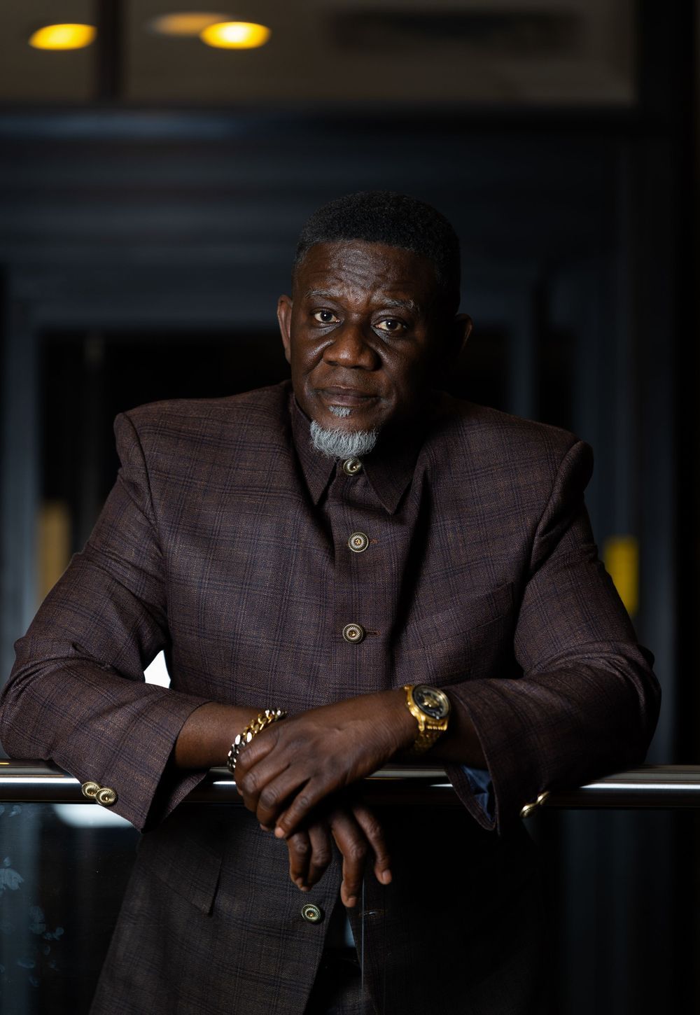 Distinguished person in dark textured blazer leans on railing while wearing elegant jewelry.