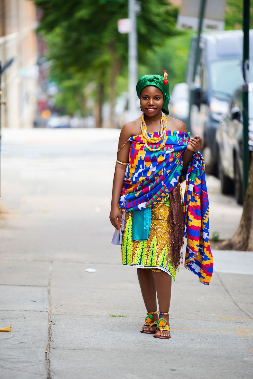 Street style photo showcasing colorful African-inspired fashion with bright prints and green headwrap.