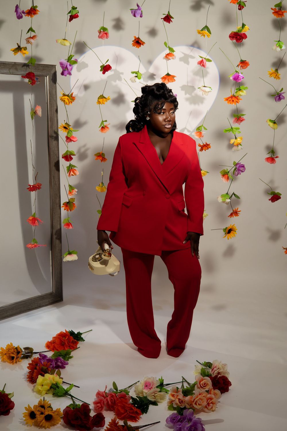 Stylish fashion photograph featuring a red suit against floral wall decorations and mirror.