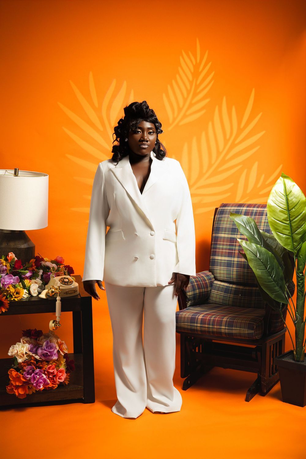 Fashionable white pantsuit captured against warm orange background with palm leaf wall art.