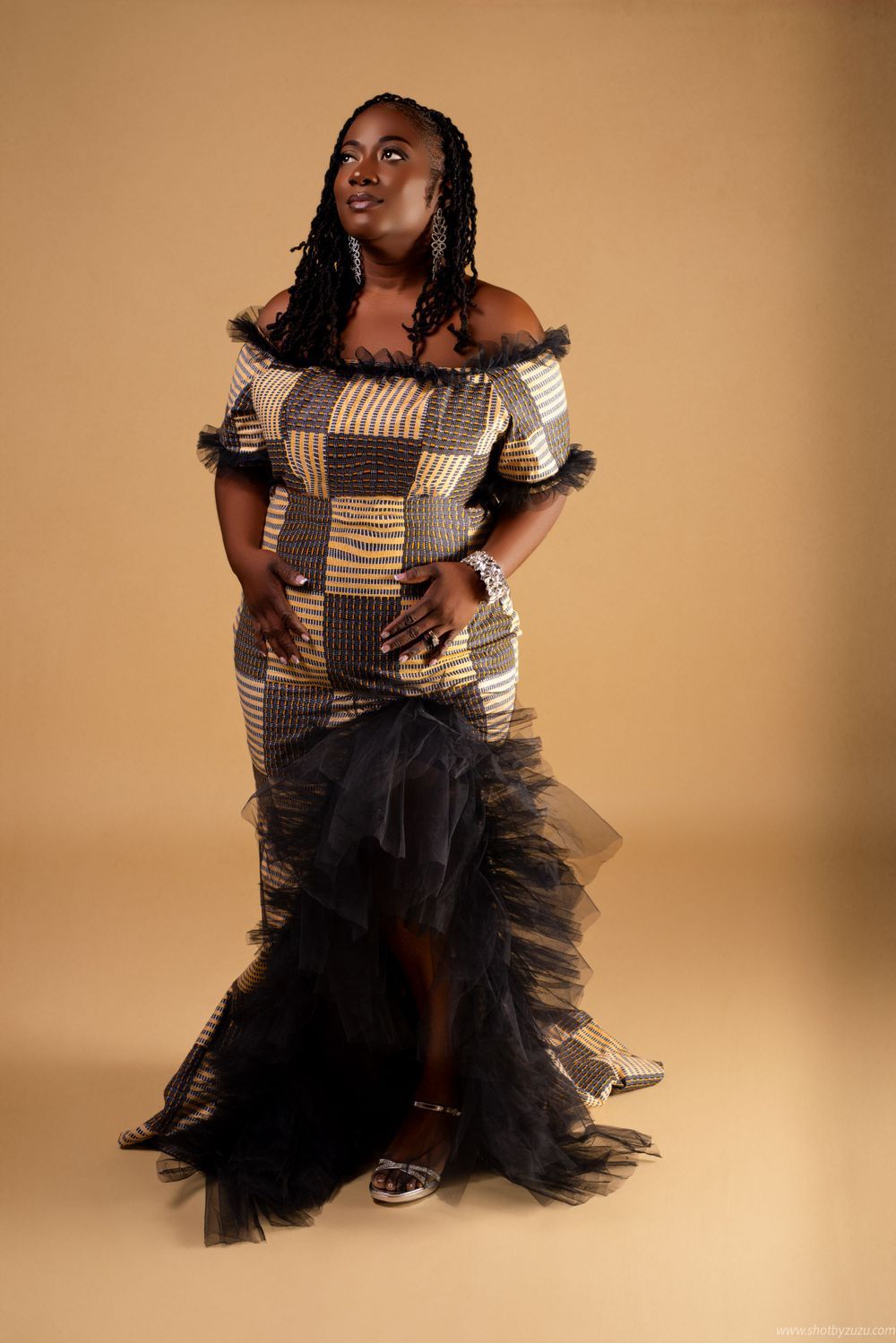 Fashion portrait in black tulle and patterned dress against warm studio background.