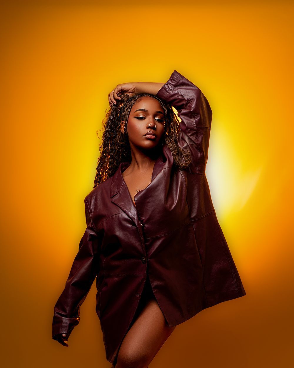 Dramatic fashion shot in burgundy leather jacket against glowing orange background.