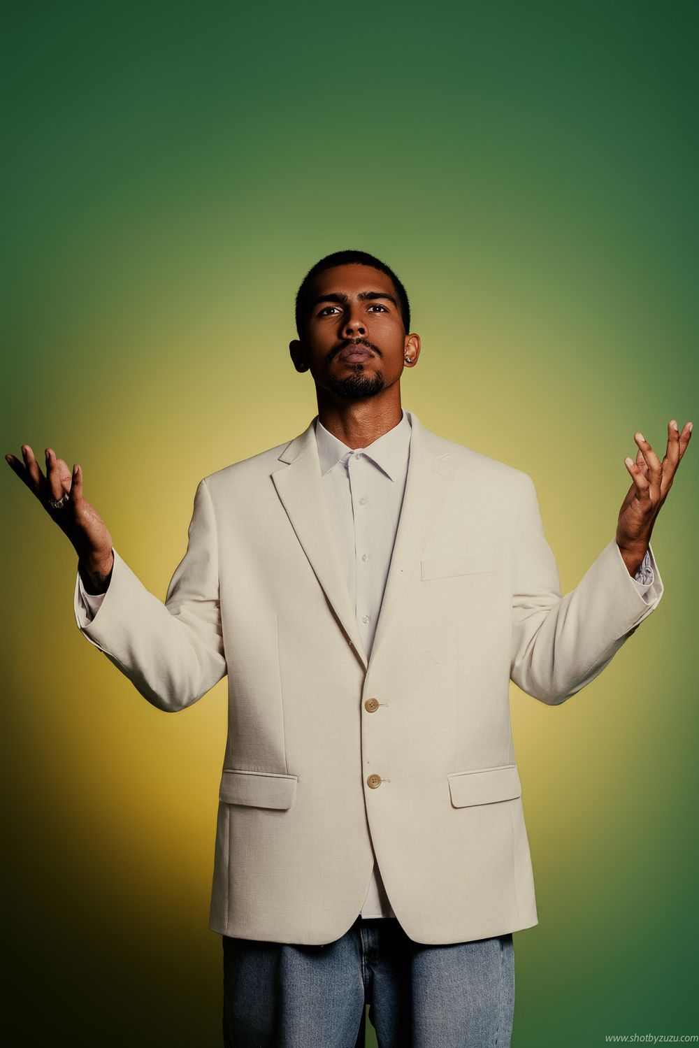 Artistic studio photo showing a person in a white suit with raised hands against a green backdrop.