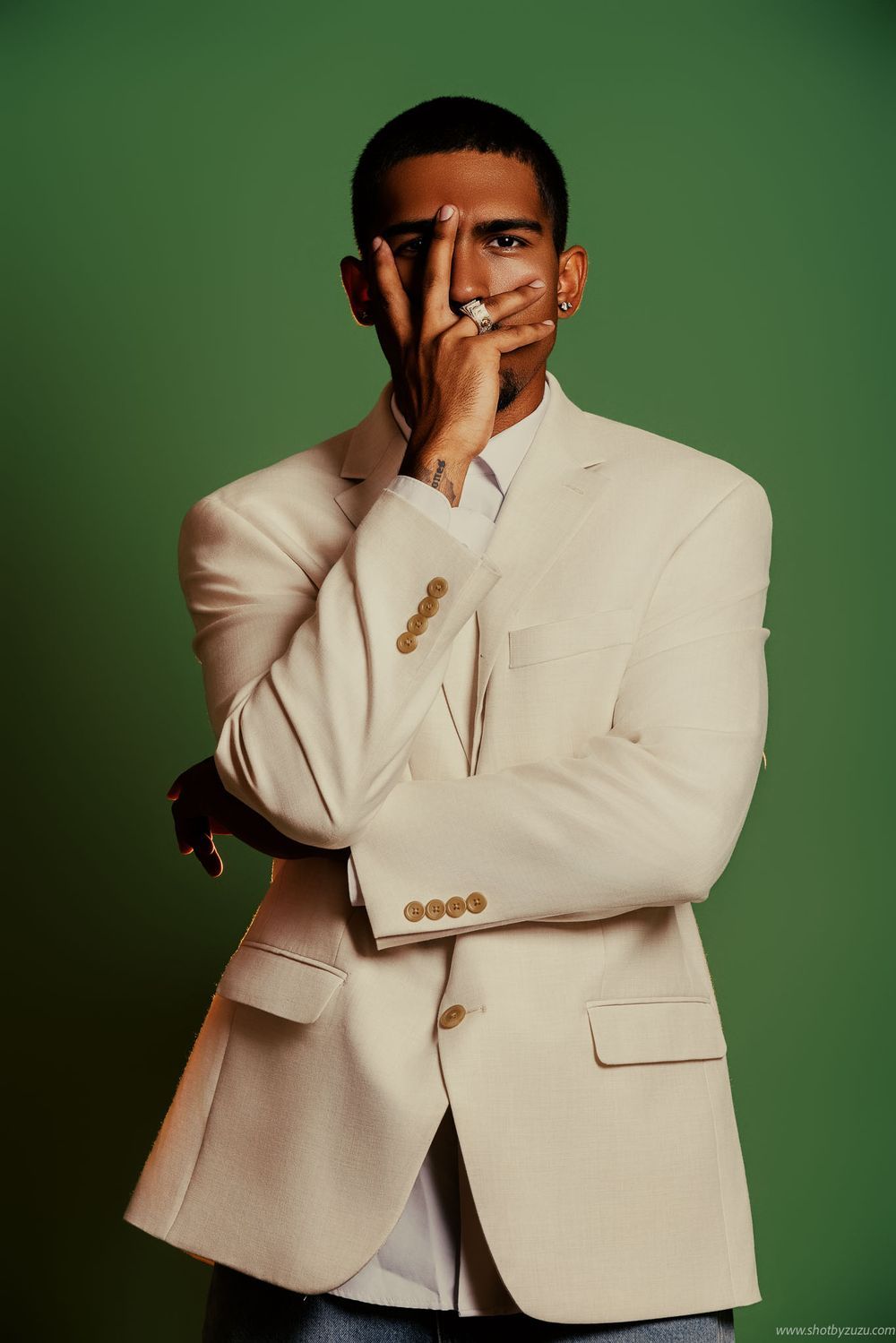 Portrait of a person in cream blazer with thoughtful pose against green background.