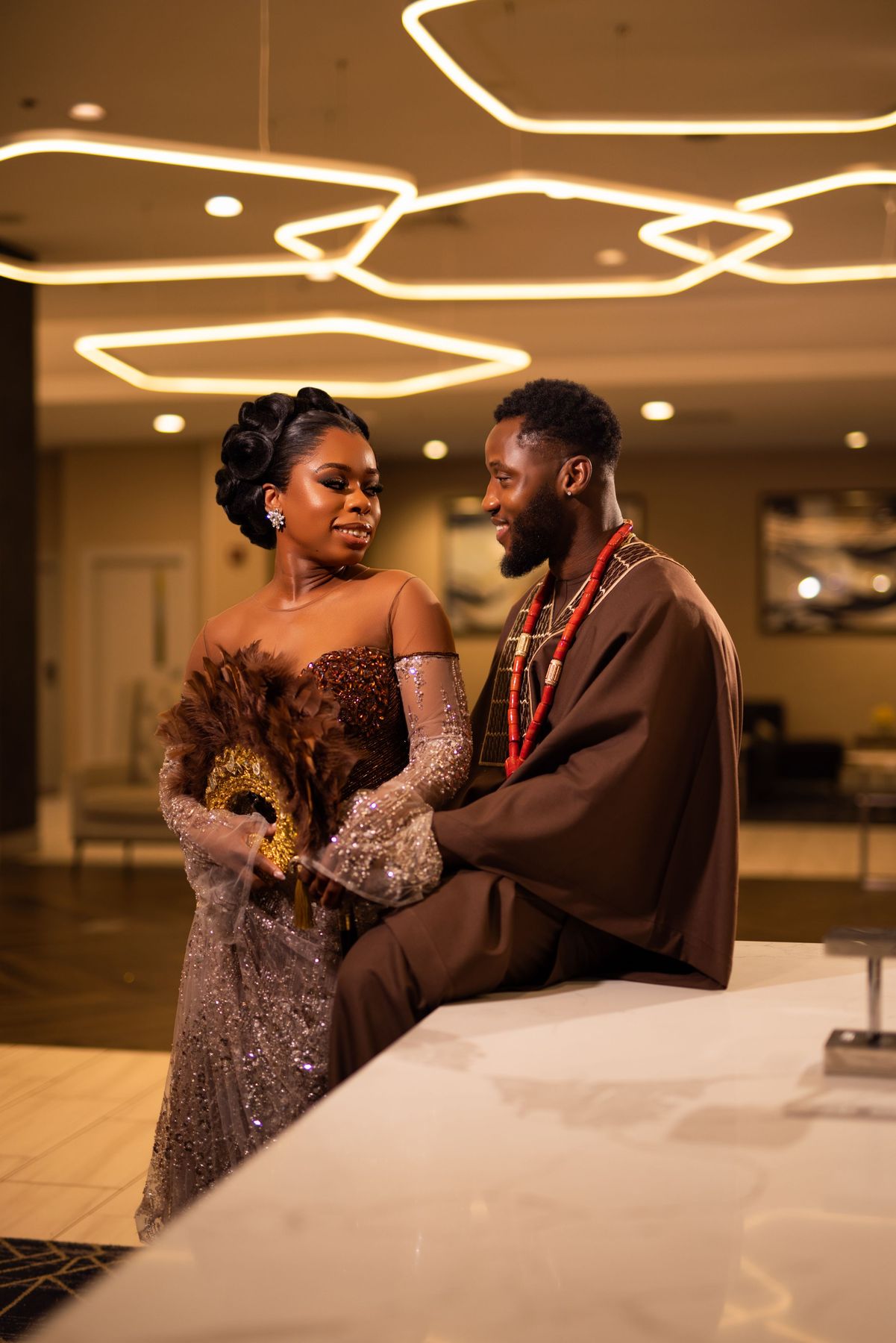 Couple shares an intimate moment at an elegant venue with decorative lighting and formal attire.