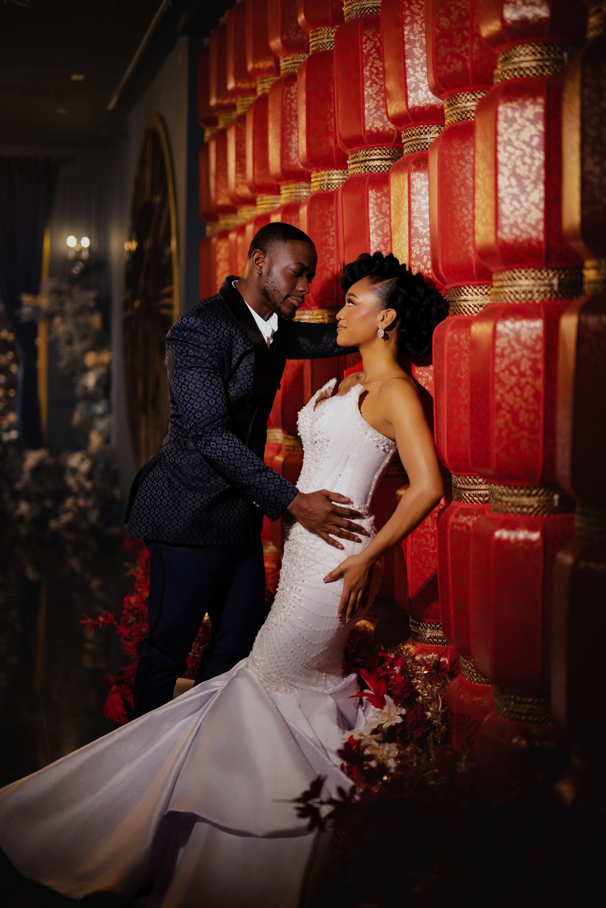 A couple shares a romantic moment in front of a vibrant red wall during their wedding photoshoot.