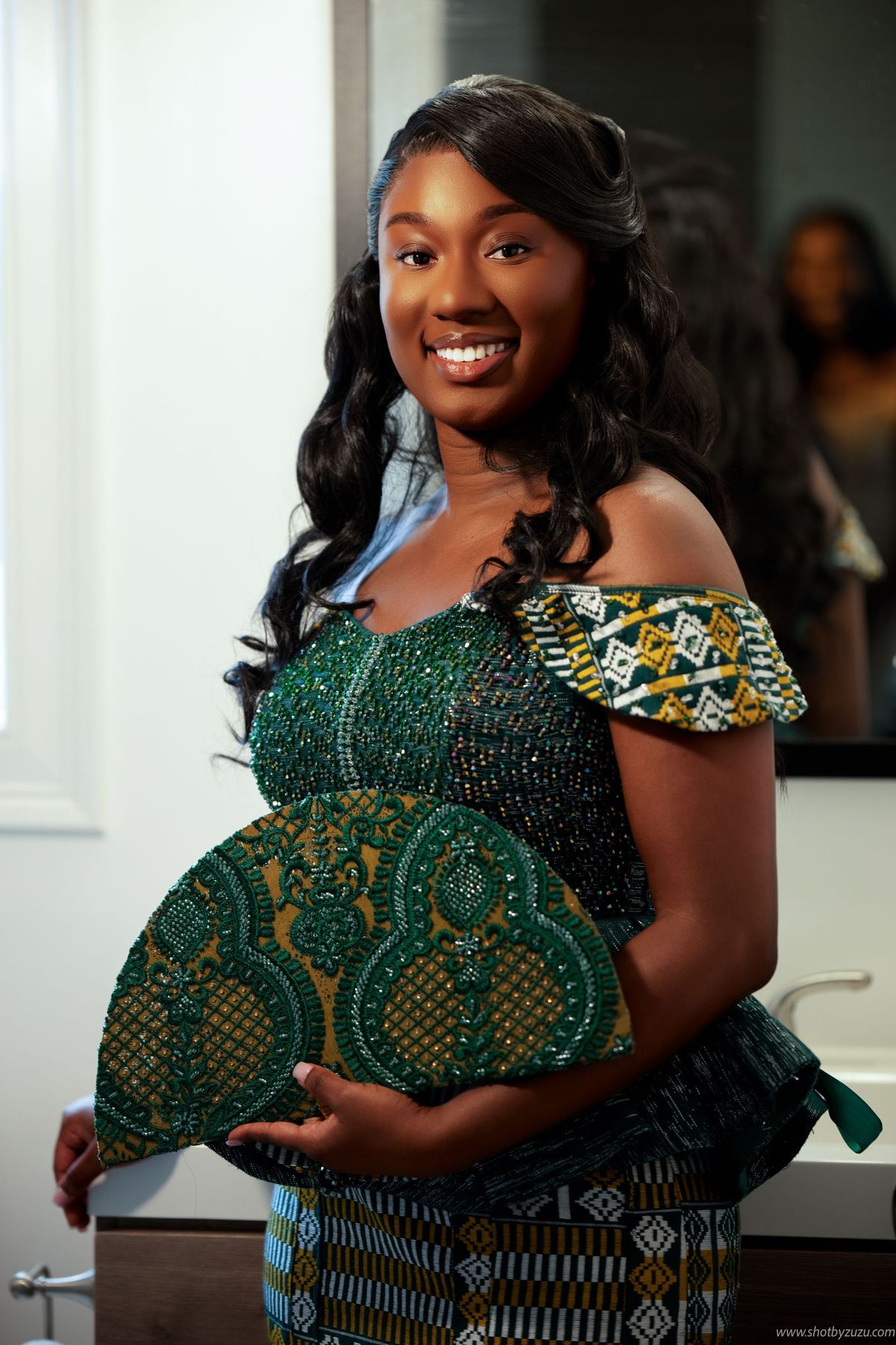 Elegant formal attire featuring green and gold African print fabric with beaded details and off-shoulder style.
